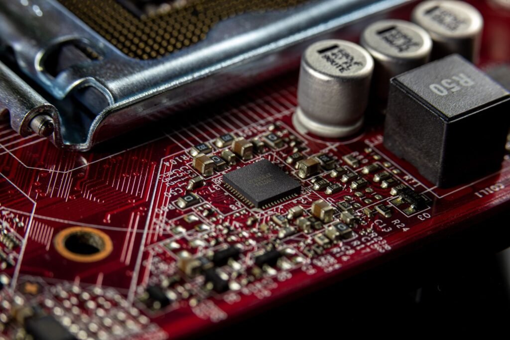 Close de uma placa de circuito vermelha com um chip preto pequeno ao centro, cercado por capacitores e resistores